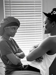 two young women sitting next to each other in front of a window with blinds on the windowsill