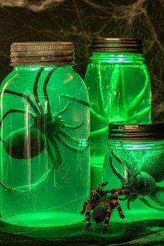 three mason jars with spider webs in them, one green and the other red