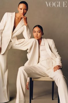 two women in white suits sitting on a chair and posing for the cover of a magazine