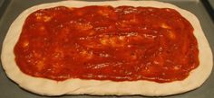 an uncooked pizza dough on a baking sheet with sauce in the middle, ready to go into the oven