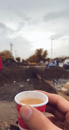 a hand holding a cup of coffee in front of a construction site with other people