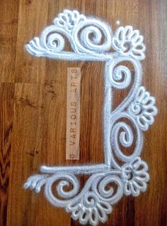 the letter l is made out of white yarn and sits on a wooden floor next to a ruler