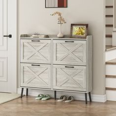 a white dresser sitting next to a stair case with shoes on it and framed pictures above the drawers