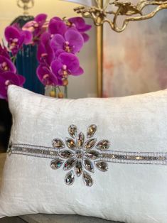 a white pillow with a crystal snowflake on the front and side, sitting on a table next to purple flowers