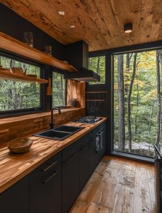 a kitchen with black cabinets and wooden counter tops in front of a large window overlooking the woods