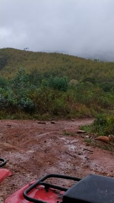 two atvs parked in the mud on a dirt road with trees and hills in the background