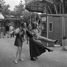 two women are posing in front of a carousel at an amusement park, one is holding the other's leg