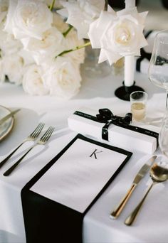 the table is set with white flowers and silverware for an elegant wedding reception in black and white