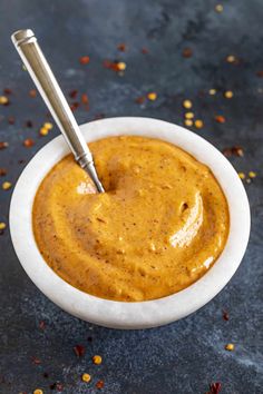 a small white bowl filled with sauce on top of a black table next to a spoon