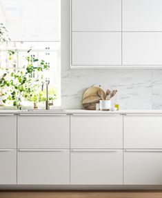 a kitchen with white cabinets and counter tops next to a potted plant on the window sill