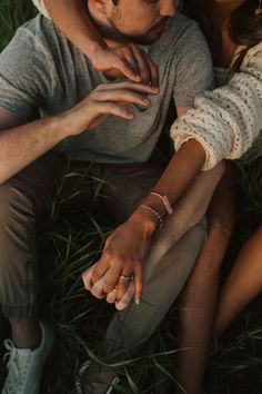 a man and woman sitting in the grass with their hands on each other's shoulders