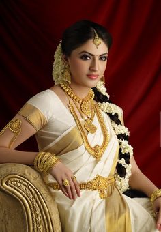 a woman in a white and gold sari sitting on a chair with her hand on her hip