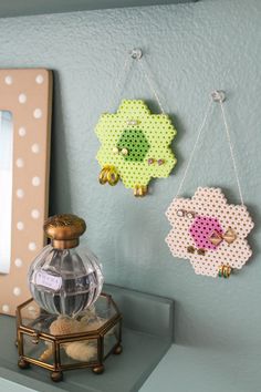 two small pieces of bead work hanging from hooks on a wall next to a mirror