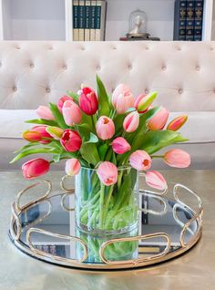 a glass vase filled with pink tulips sitting on top of a metal tray