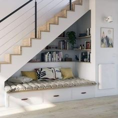 there is a bench under the stairs with books on it and some pillows in front