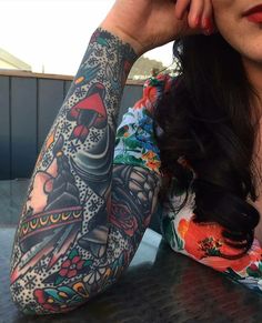 a woman sitting at a table with tattoos on her arm and arms behind her head