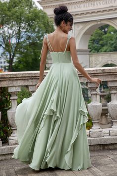 a woman in a long green dress is standing on a stone wall with her back to the camera