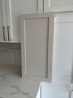 a white kitchen with marble counter tops and cabinets in the backround, next to a light switch