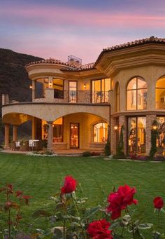 a large house in the middle of a lush green field with red flowers on it