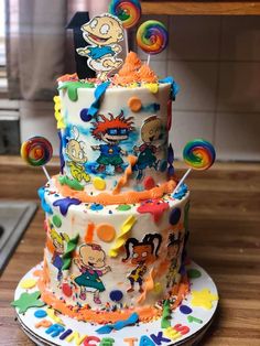 a multi - tiered cake decorated with cartoon characters and rainbow colored icing on a wooden table