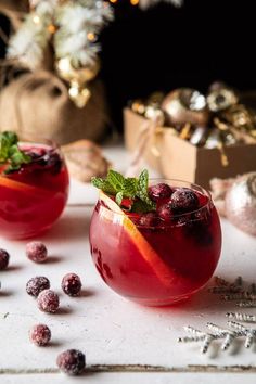 two glasses filled with fruit and garnish on top of a white table next to christmas decorations