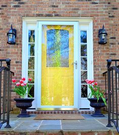 a yellow front door with two flower pots on the steps