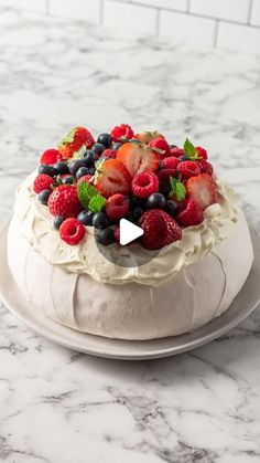 a cake with berries and mints on top sitting on a marble counter next to a white brick wall