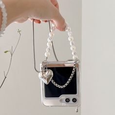 a hand holding a cell phone with a chain attached to it and a heart charm hanging from the back