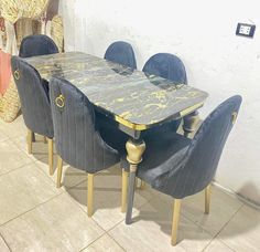 a dining table with blue velvet chairs and a gold leaf design on the top, in front of a white wall