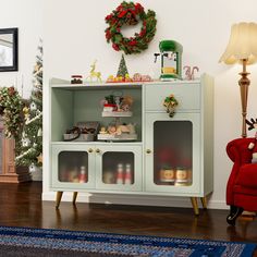 a living room with a christmas wreath on the wall next to a green cabinet and red chair