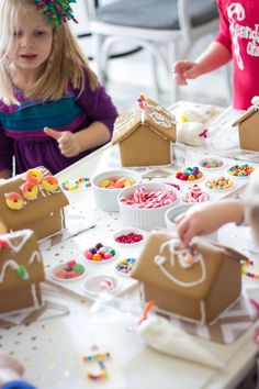 two children at a table with gingerbread houses and other desserts on the table