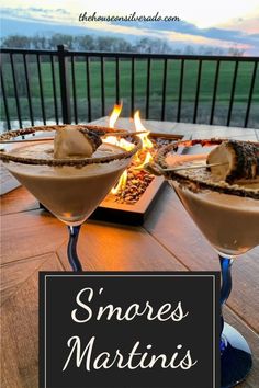 two martinis sitting on top of a wooden table next to a fire pit with marshmallows