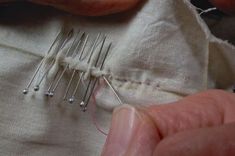 someone is stitching something on a piece of cloth with pins and needles in their hands