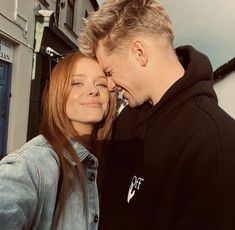 a man and woman standing next to each other in front of a building with their eyes closed