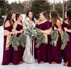 a group of women standing next to each other in the snow wearing dresses and holding wreaths