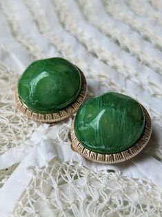 two green buttons sitting on top of a white lace covered table cloth next to each other