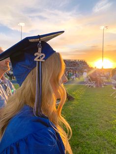 a woman wearing a blue graduation cap and gown looking into the distance at a sunset