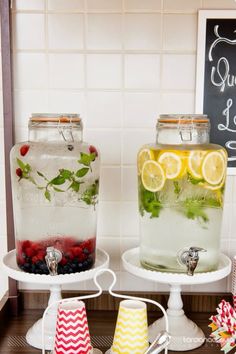 two jars with lemons, raspberries and water are sitting on serving trays