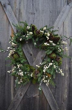 a wreath is hanging on the side of a wooden fence with white flowers and pine cones