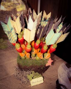 an arrangement of fruit and feathers in a vase on a table with a name tag