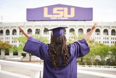 a woman in purple graduation gown and cap raising her arms up with the lsu stadium in the background