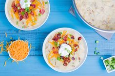 three bowls filled with food on top of a blue wooden table next to green onions and cheese