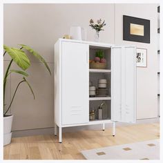 a white cabinet sitting on top of a wooden floor next to a potted plant