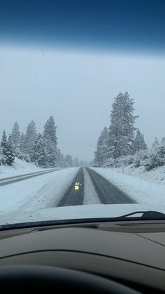 a car driving down a snow covered road in the middle of winter with trees on both sides