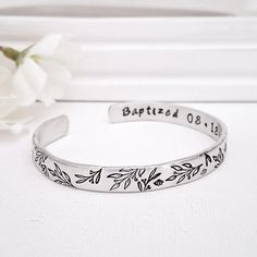 This floral themed  bracelet is a pretty way to celebrate an adult baptism! The inside will be hand stamped with the word Baptized and a date as shown, but a name can also be added to the other inside cuff end to create a personalized keepsake that any woman or teen girl will love. The outside of the cuff will be stamped with floral and branch design shown. Each piece is created by hand so pattern may vary a bit. Bracelet is made of lightweight aluminum which will never tarnish. It is slightly a Silver Bracelet For Baptism Mother's Day, Adjustable Name Bracelet With Engraving Option For Wedding, Adjustable Birth Flower Bracelet For Wedding, Adjustable Hand Stamped Wedding Bracelets, Adjustable Hand Stamped Bracelets For Wedding, Personalized Silver Name Bracelet For Baptism, Personalized Adjustable Bracelet For Baptism, Personalized Adjustable Bracelets For First Communion, Adjustable Silver Name Bracelet For Baptism