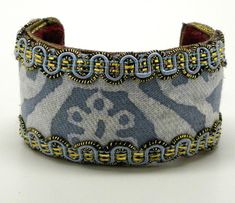 a blue and white cuff bracelet with gold chains on it's sides, decorated with an ornate design