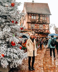 a woman standing next to a christmas tree in front of a building with lots of decorations