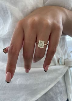 a woman's hand wearing a gold ring with a square shaped diamond on it