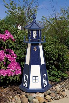 a blue and white light house sitting on top of a pile of rocks next to purple flowers