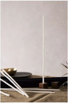 two white candles sitting on top of a table next to chopsticks and a plate